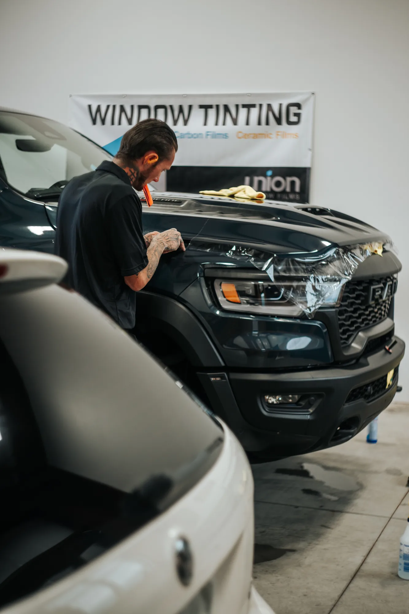 Installer at the nose of a Ram truck, telephoto compression inside the tint shop