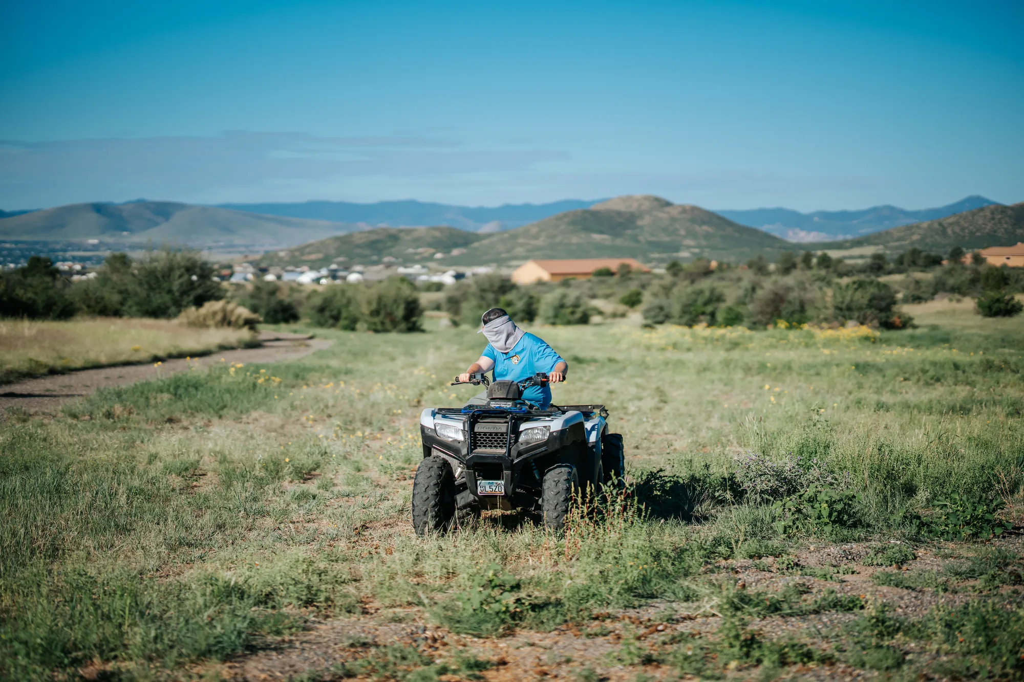 Scoop & Skedaddle team member riding an ATV across a pasture with mountains on the horizon