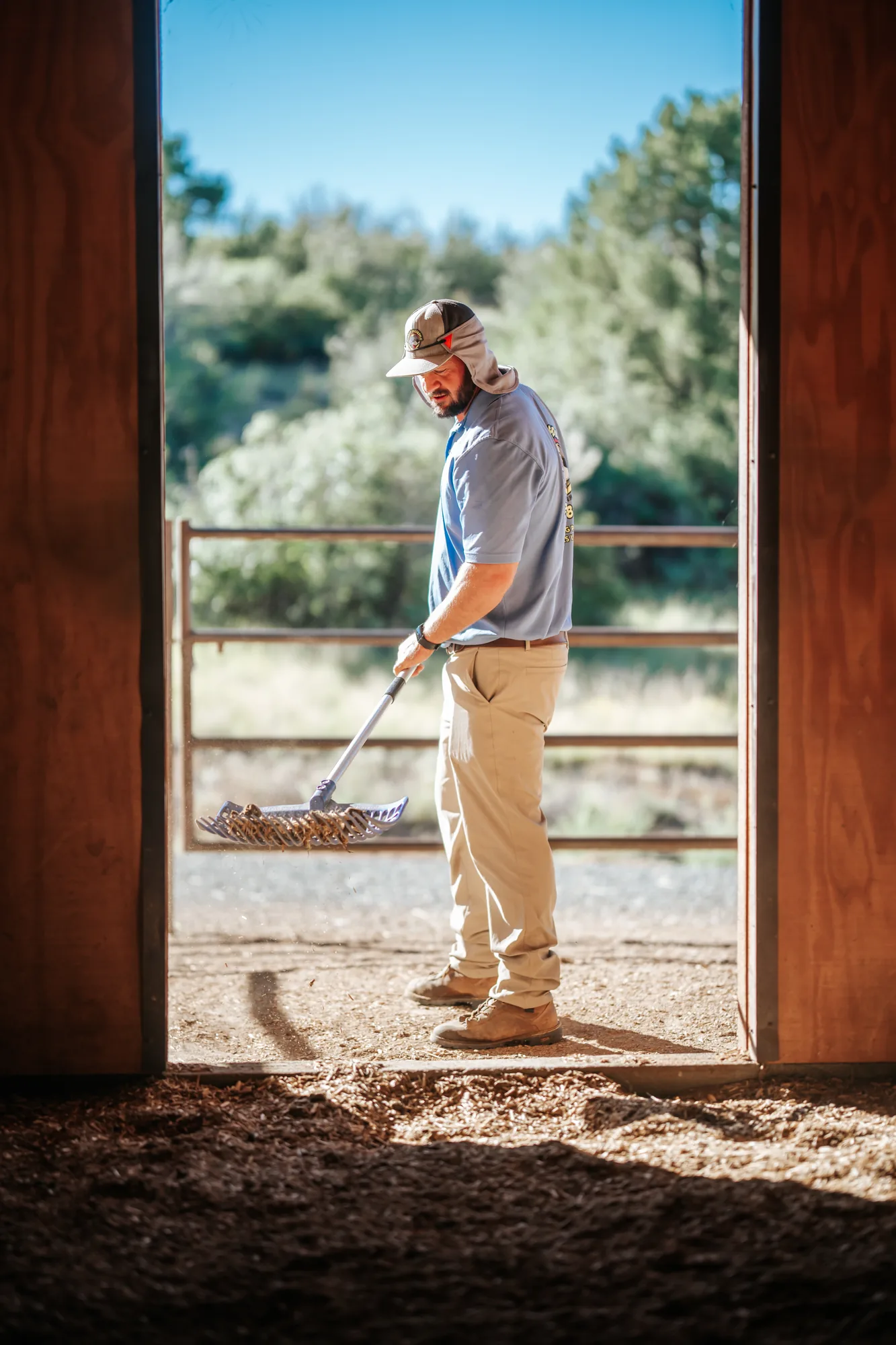 Scoop & Skedaddle team member raking a stall entrance, framed by a barn doorway