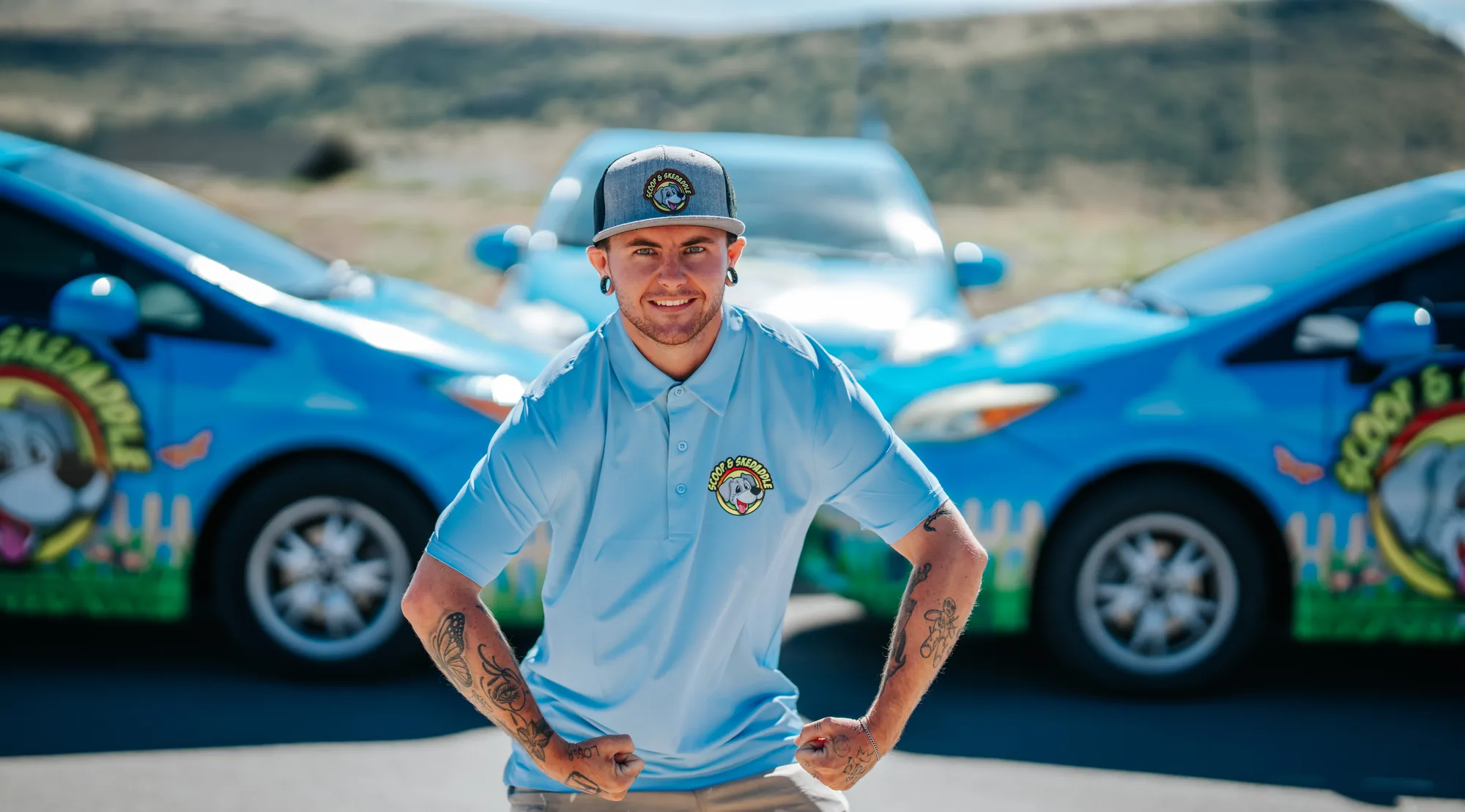 Portrait of a Scoop & Skedaddle crew member with hands on hips in front of the company cars