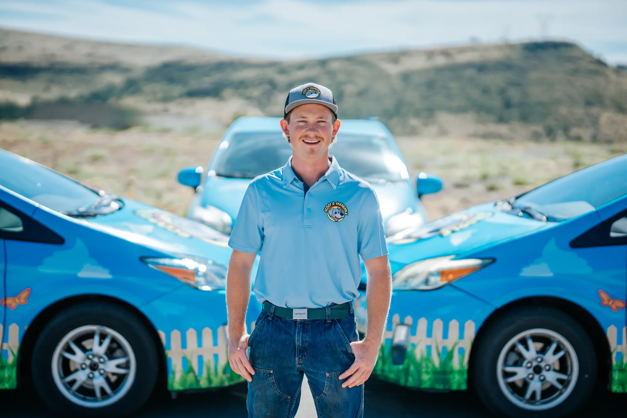 Portrait of a Scoop & Skedaddle crew member standing between two company cars