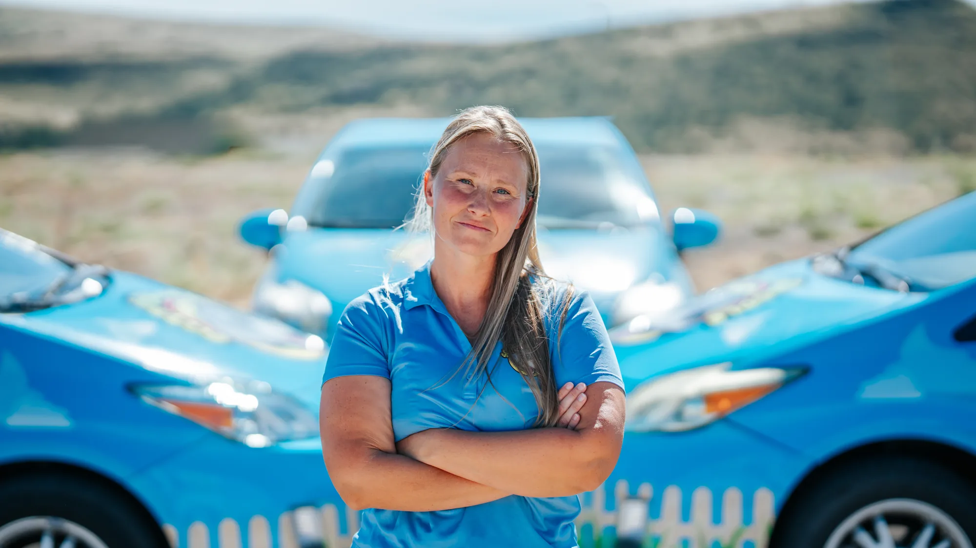 Portrait of a Scoop & Skedaddle crew member with arms crossed in front of the company cars