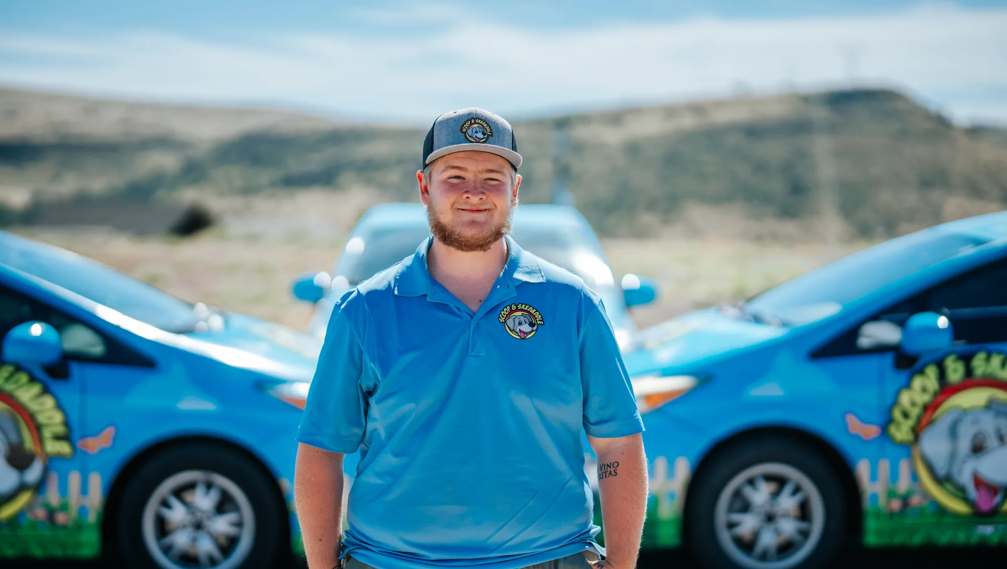 Portrait of a Scoop & Skedaddle crew member smiling in front of the company cars