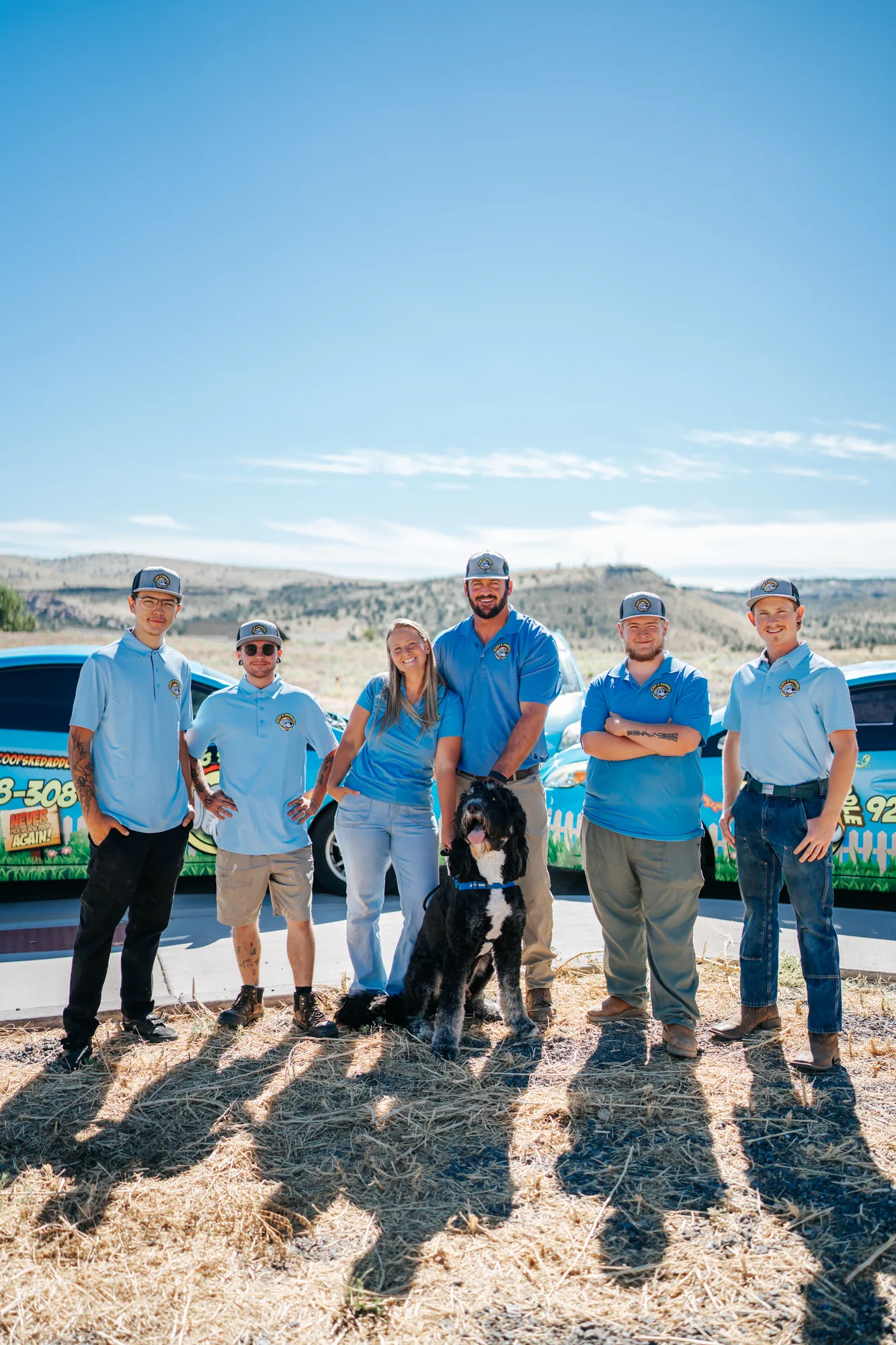 The six-person Scoop & Skedaddle crew and their dog standing in front of the wrapped company cars