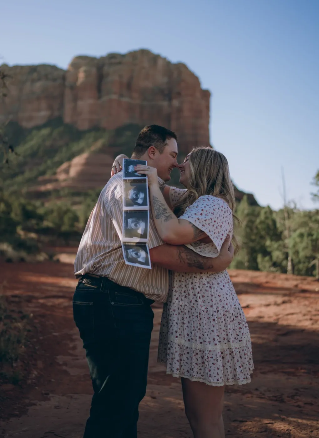 A couple embracing and holding an ultrasound photo for a baby announcement in Sedona's red rock country, photographed by Tex Kelly