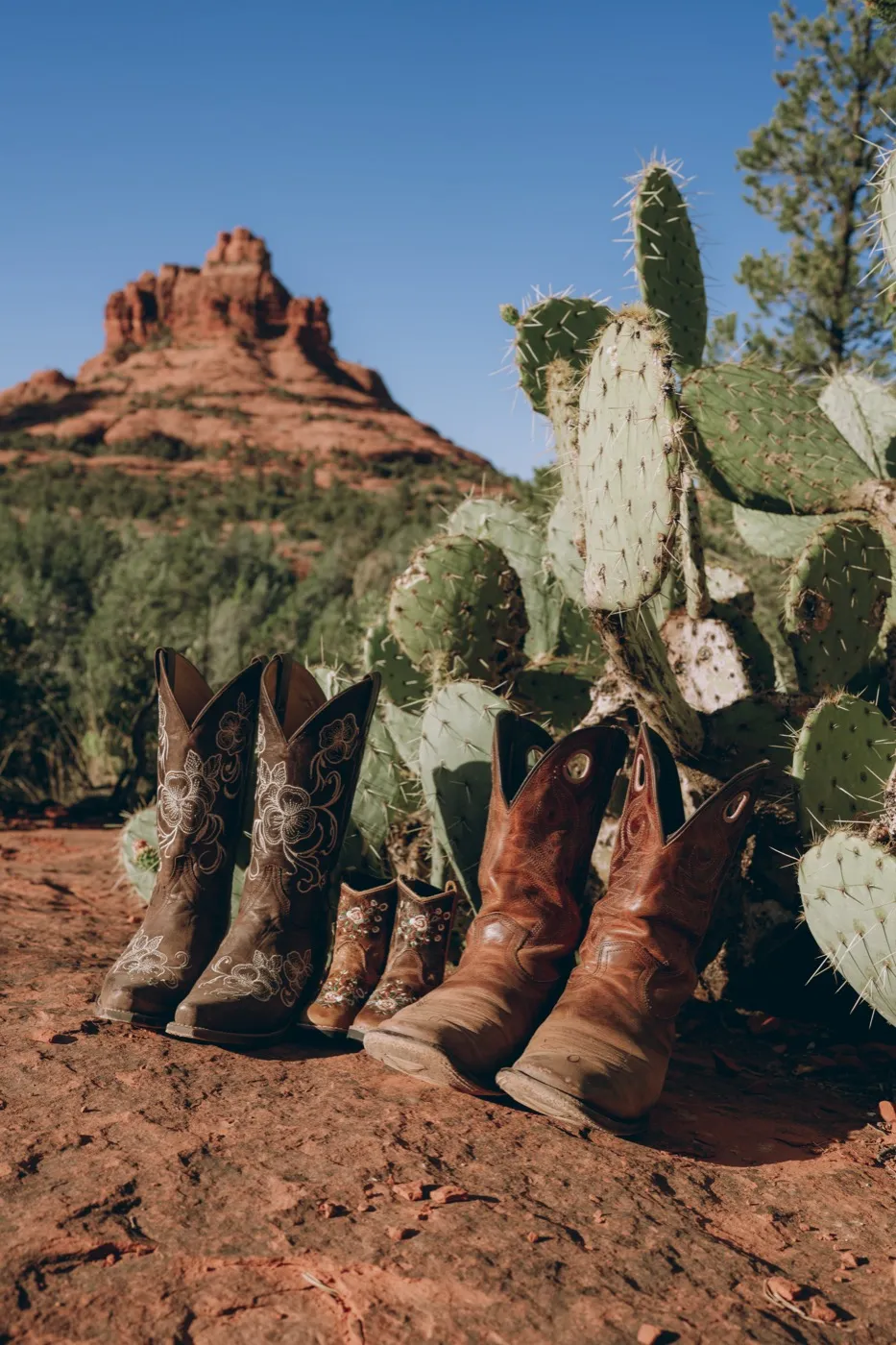 Sedona pregnancy announcement, three pairs of cowboy boots below Bell Rock. Photography by Tex Kelly Productions, serving Sedona, Arizona.