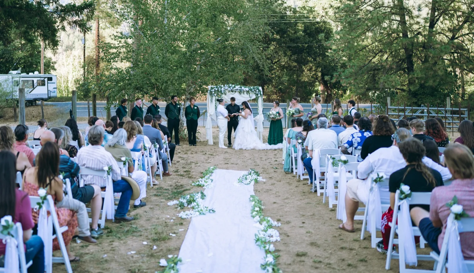 Wide outdoor ceremony with floral aisle and pine-grove backdrop. North Coast wedding