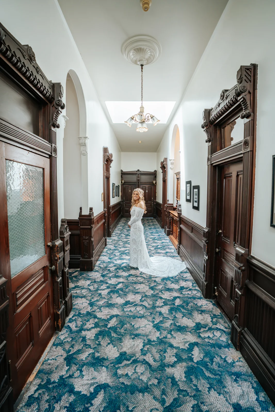 Bride walking a long Victorian hallway with carved wood doorways and patterned carpet