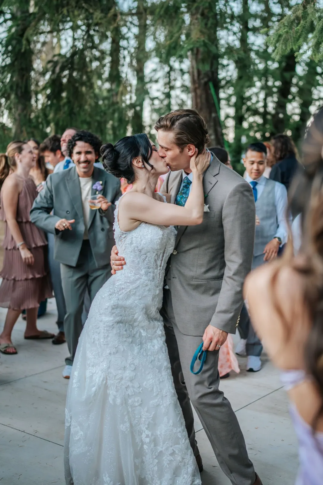 Bride and groom kiss as guests dance behind, outdoor reception wedding