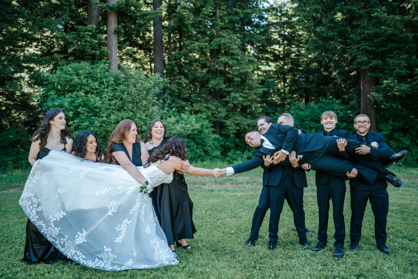 Bridesmaids lift the bride while groomsmen hoist the groom in a playful wedding party portrait on the lawn