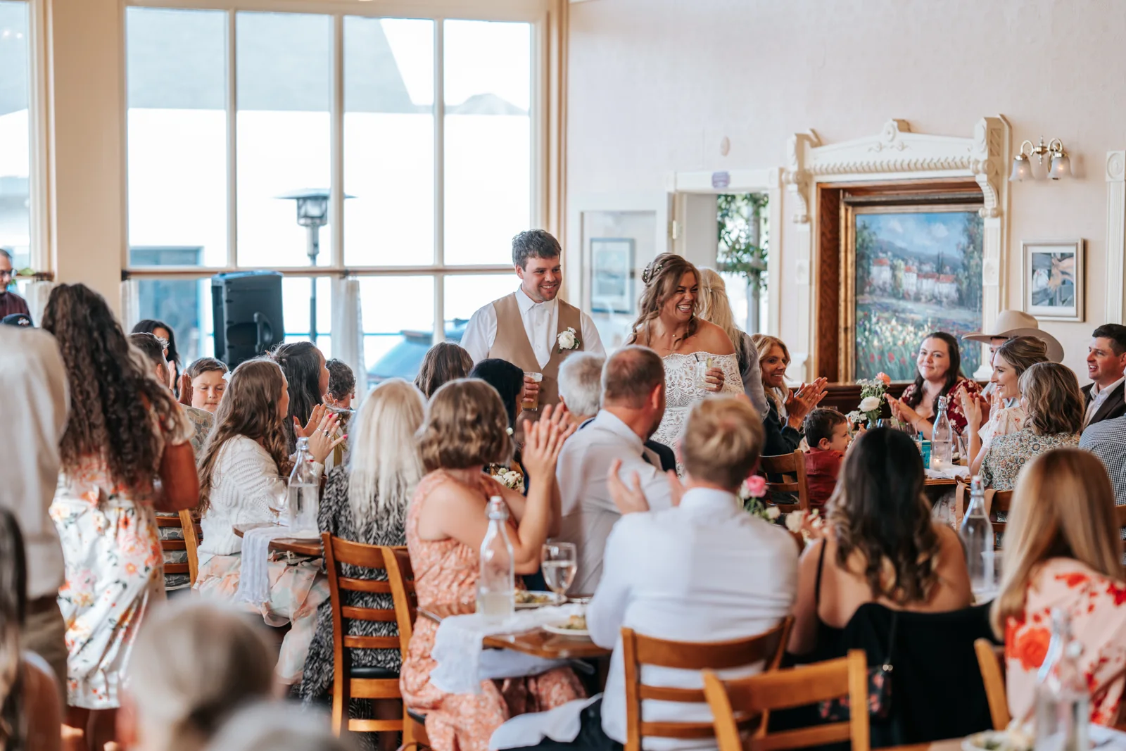 Bride and groom make their grand entrance as seated reception guests cheer and applaud