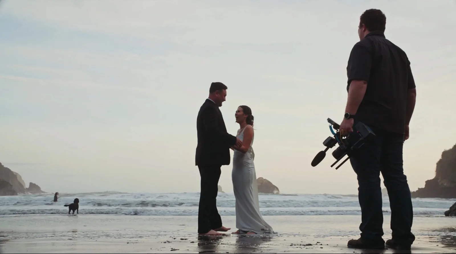 Beach ceremony at sunset with videographer in frame. North Coast wedding