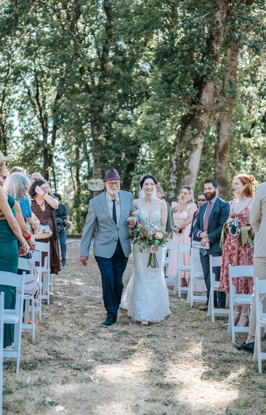 Bride walking the aisle with her father under the trees