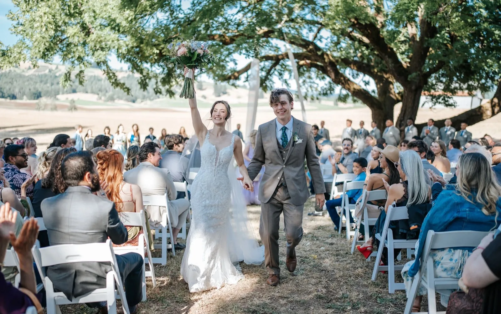 Bride and groom walking the aisle under a redwood with celebrating guests