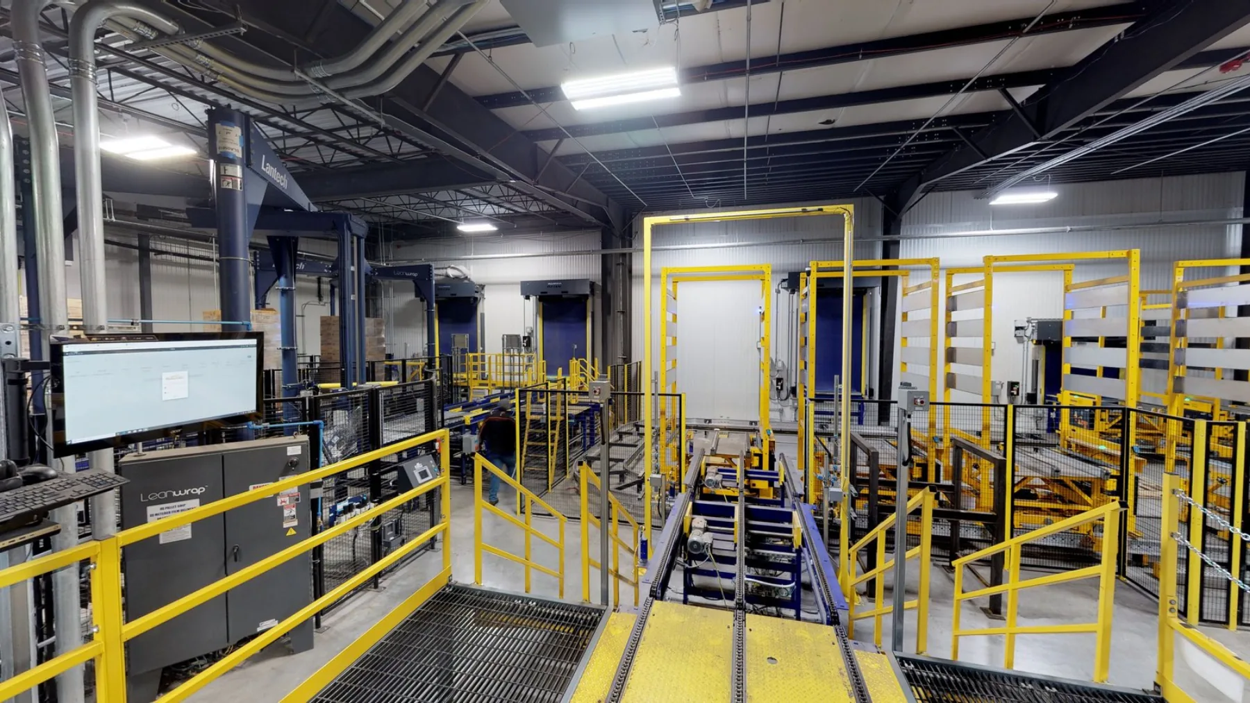 Manufacturing facility with yellow safety railings, packaging line, and overhead utility runs (photo via Matterport partner materials)
